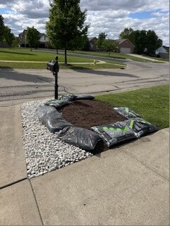 Mailbox garden bed with soil, bags of material and a white-stone border